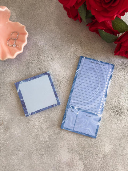 Two blue notepads on a textured surface with red flowers and a pink dish in the background.